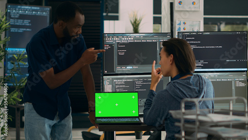 Diverse app developers working with greenscreen on laptop and programming source code with html script on monitor. Looking at isolated mockup template with chromakey display, copyspace.