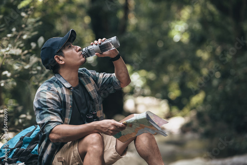 The trekker was looking at the map to find the hiking trails at the stream and drink water in the forest. hiking and adventure concept..