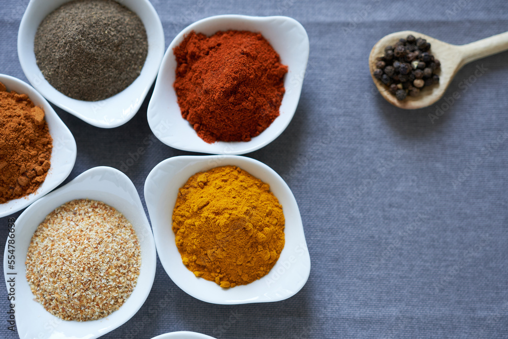 A variety of spices in white bowls on a gray background. The concept is spices for cooking meat dishes.