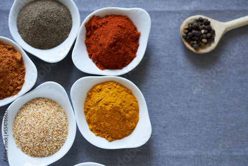 A variety of spices in white bowls on a gray background. The concept is spices for cooking meat dishes.