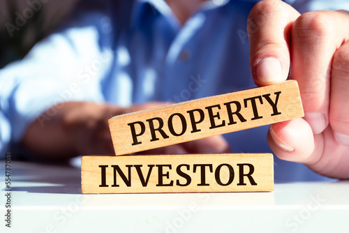 Closeup on businessman holding a wooden blocks with text PROPERTY INVESTOR, business concept