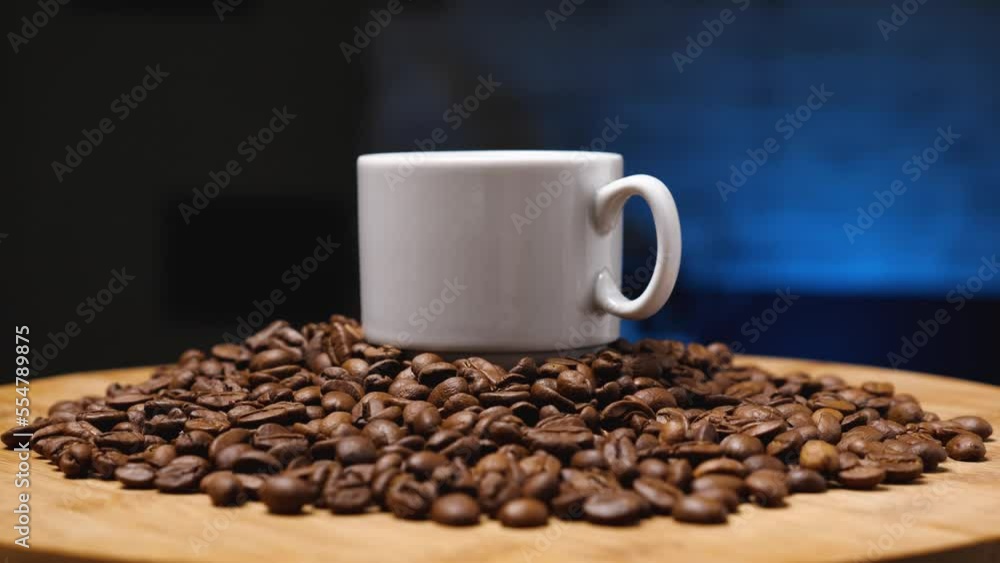A white ceramic mug surrounded by roasted coffee beans on a wooden surface. Camera rotates around. Close-up. Dark blue background. Coffee shop concept. Parallax effect A white ceramic mug surrounded by roasted coffee beans on a wooden surface. Camera rotates around. Close-up. Dark blue background. Coffee shop concept. Parallax effect