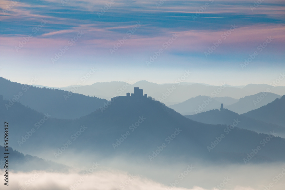Fototapeta premium Herbstliches Panorama vom Pfälzerwald mit Berggipfeln und Tälern im Nebel. In der Bildmitte sieht man die Burg Trifels bei Annweiler