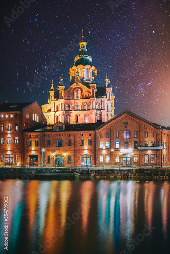 Helsinki, Finland. Bright Starry Rotation Sky. View Of Kanavaranta Street With Uspenski Cathedral In Evening Night Illuminations. Stars Movement Lines.