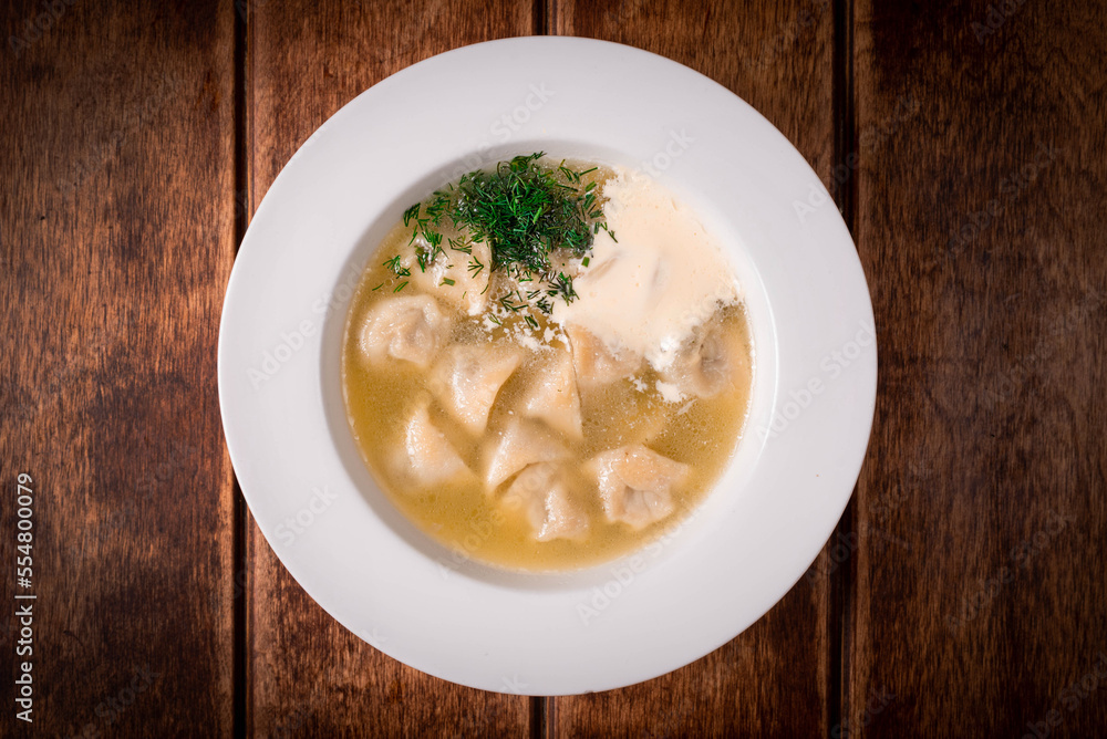 dumplings with broth and sour cream on a wooden background dumplings with broth and sour cream on a wooden background