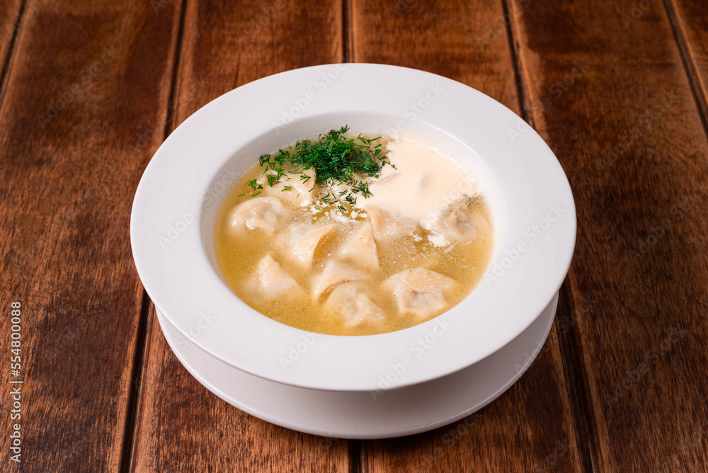 dumplings with broth and sour cream on a wooden background