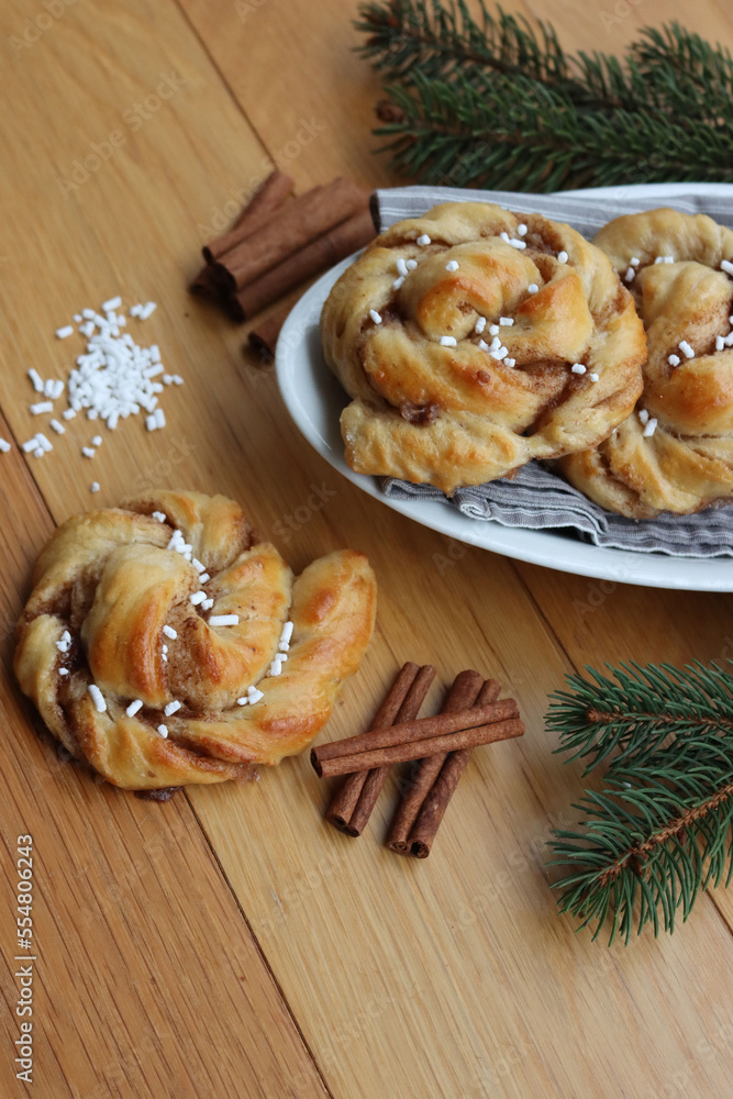 Kanelbullar, traditional swedish cinnamon and cardamon buns on wooden table with pine branche decorations