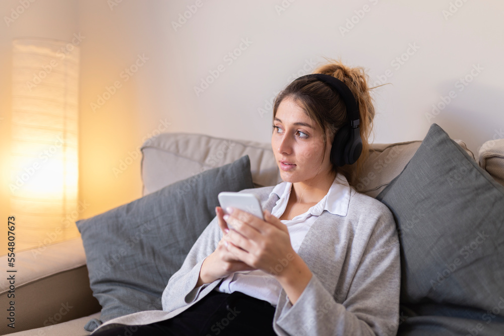 Thoughtful woman with smart phone sitting on sofa at home Thoughtful woman with smart phone sitting on sofa at home