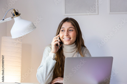 Smiling young woman talking on smart phone at home