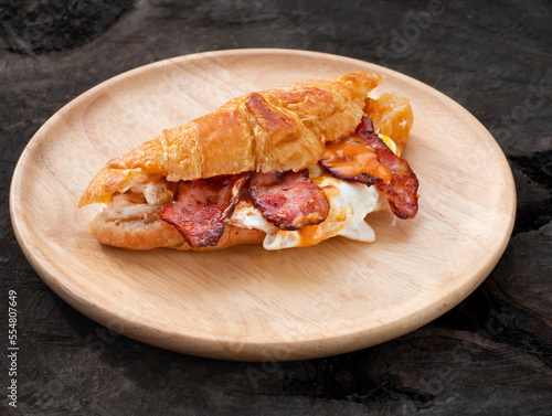 Croissant sandwich breakfast with egg and crispy bacon on plate.
