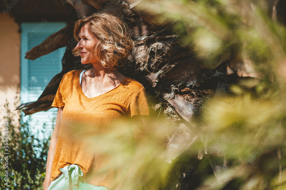 Smiling mature woman standing in front of tree on sunny day Smiling mature woman standing in front of tree on sunny day