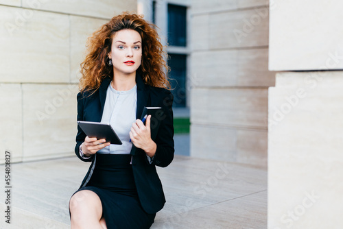 Tableau sur toile Horizontal portrait of pretty confident businesswoman dressed formally, holding her pocket book with pen and tablet computer, being busy with her work
