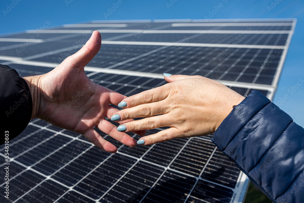 Two people shaking hands against a solar panel after signing a renewable energy deal.