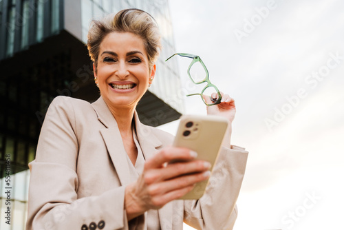 Mature grey woman smiling and using mobile phone on balcony