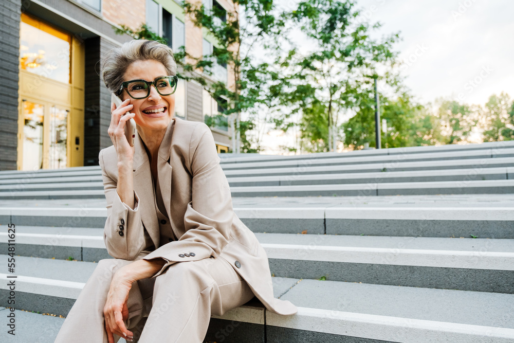 Mature woman talking on cellphone while sitting on stairs by building