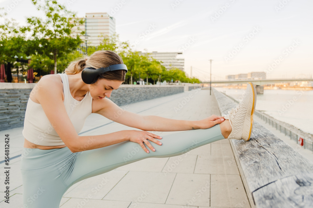 Young sportswoman listening to music while doing workout at embankment