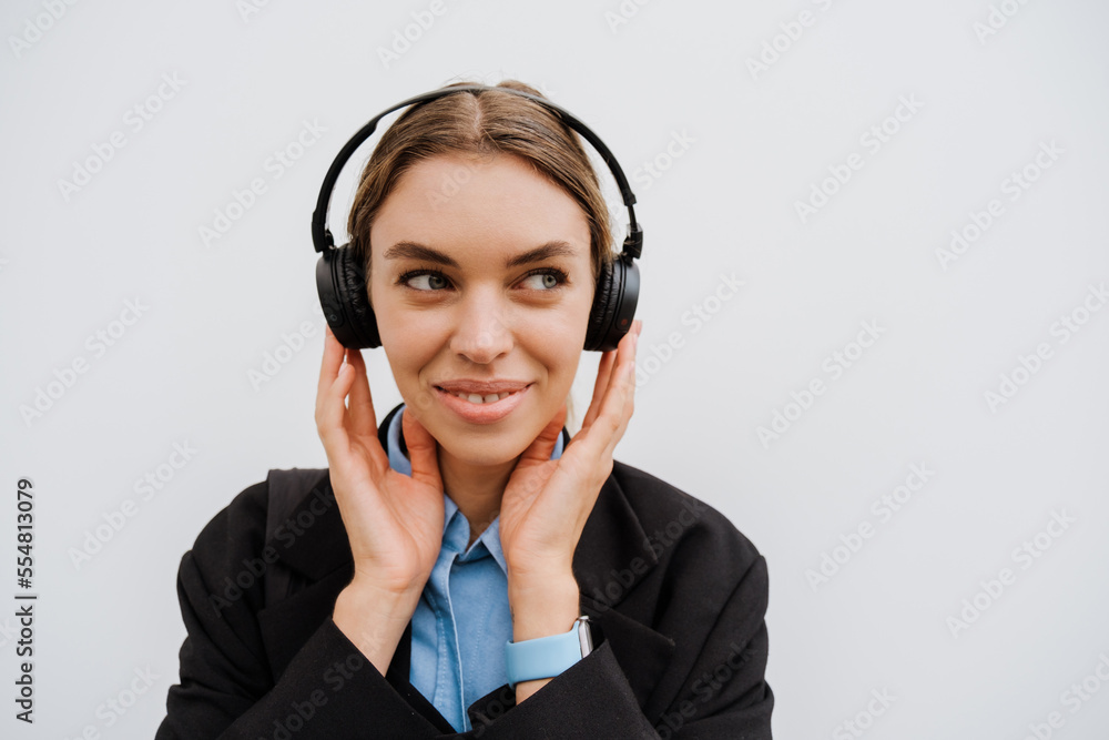 Young woman in headphones smiling while standing over white wall Young woman in headphones smiling while standing over white wall