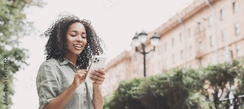 Young beautiful woman using smartphone in a city panoramic banner. Smiling student girl texting on mobile phone outdoor.  Modern lifestyle, connection, casual business concept