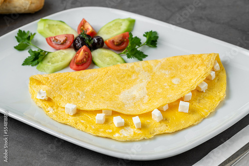 Feta cheese omelet with olives and tomatoes on a white porcelain plate