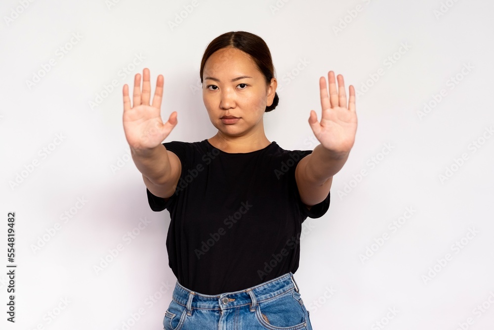 Portrait of confident young woman making denial gesture over white background. Asian lady wearing black T-shirt and jeans stretching arms in stop gesture. Forbiddance concept Portrait of confident young woman making denial gesture over white background. Asian lady wearing black T-shirt and jeans stretching arms in stop gesture. Forbiddance concept