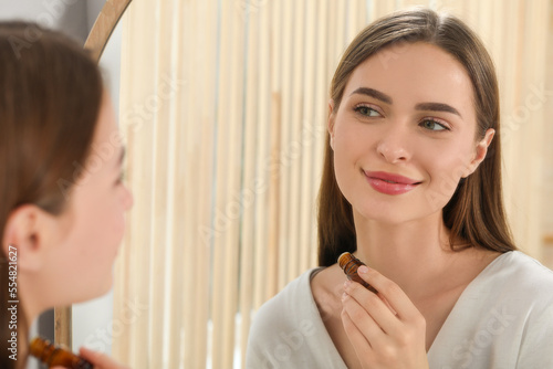 Young woman applying essential oil onto neck indoors