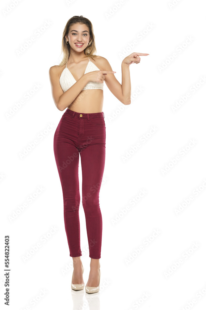 Smiling Woman In Burgundy Jeans And Top Presenting Something ,Touching, Showing Direction On A White Background Smiling Woman In Burgundy Jeans And Top Presenting Something ,Touching, Showing Direction On A White Background