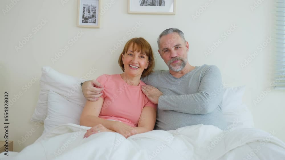 Portrait of Caucasian senior elderly couple sitting on bed in bedroom Portrait of Caucasian senior elderly couple sitting on bed in bedroom