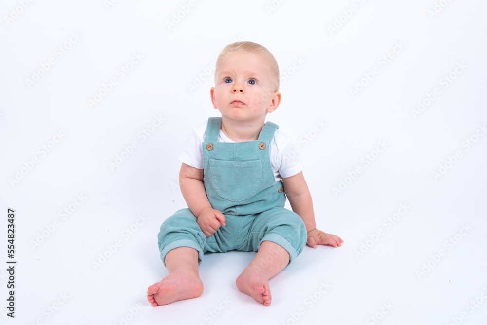 Close-up portrait of beautiful baby boy wearing light blue jumpsuit over white studio background smiling and looking aside. Close-up portrait of beautiful baby boy wearing light blue jumpsuit over white studio background smiling and looking aside.