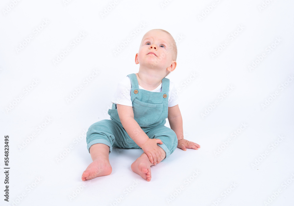 Close-up portrait of beautiful baby boy wearing light blue jumpsuit over white studio background smiling and looking aside. Close-up portrait of beautiful baby boy wearing light blue jumpsuit over white studio background smiling and looking aside.