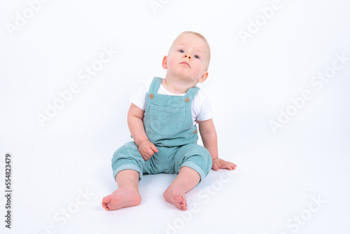 Close-up portrait of beautiful baby boy wearing light blue jumpsuit over white studio background smiling and looking aside. 