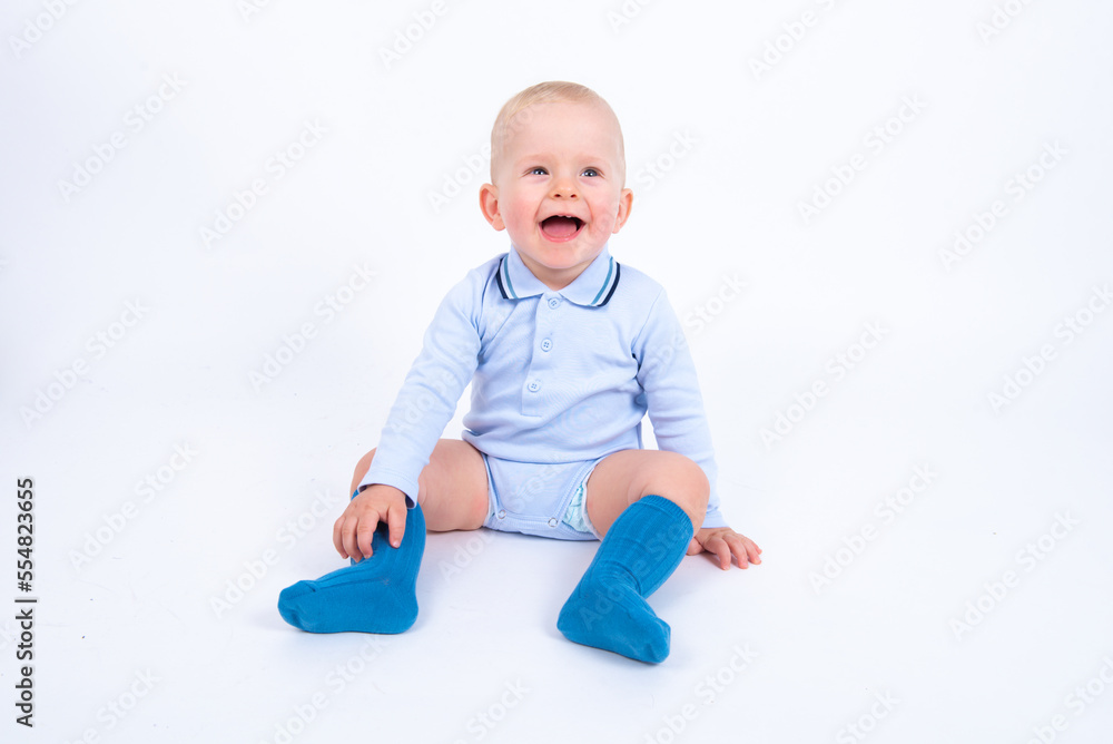 Beautiful blond baby boy wearing blue sitting against white background, laughing and looking up. Advertisement concept. 