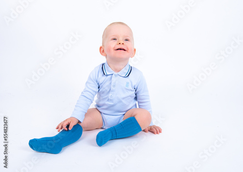 Beautiful blond baby boy wearing blue sitting against white background, smiling and looking up. Advertisement concept. 