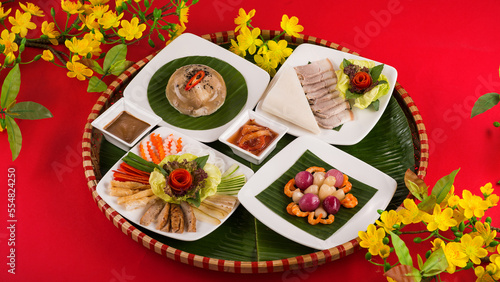 Family dinning table of Tet holiday or Lunar New Year with traditional foods: pork belly and eggs braised in coconut water, pickles, rice, Banh Tet (rice cake), fried vegetables, bitter melon soup. 