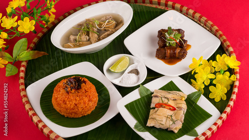 Family dinning table of Tet holiday or Lunar New Year with traditional foods: pork belly and eggs braised in coconut water, pickles, rice, Banh Tet (rice cake), fried vegetables, bitter melon soup. 