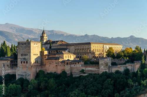 Picturesque scenery of ancient Alhambra Palace located on top of hill covered with lush green trees against cloudless blue sky on sunny day in Granada