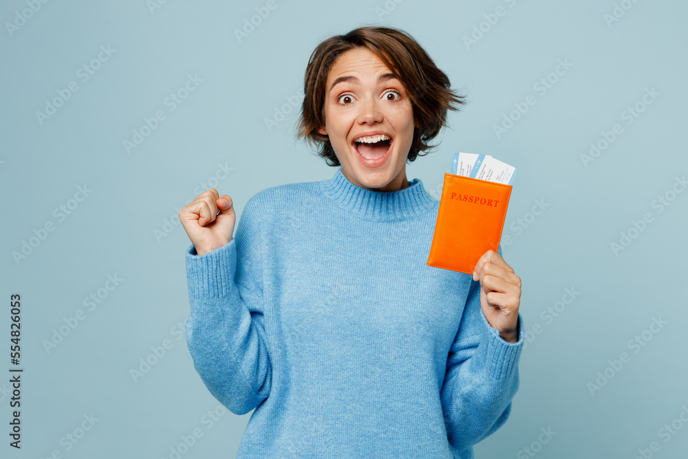 Traveler woman wear sweater hold passport ticket do winner gesture isolated on plain light blue cyan background Tourist travel abroad in free spare time rest getaway Air flight trip journey concept. Traveler woman wear sweater hold passport ticket do winner gesture isolated on plain light blue cyan background Tourist travel abroad in free spare time rest getaway Air flight trip journey concept.