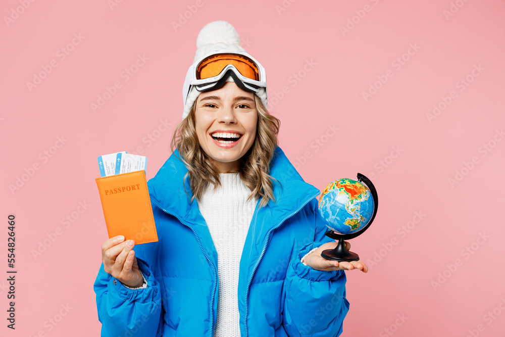 Snowboarder woman inblue suit goggles hat ski jacket hold passport ticket globe isolated on plain pink background. Tourist travel abroad in free spare time rest Air flight winter trip sport concept Snowboarder woman inblue suit goggles hat ski jacket hold passport ticket globe isolated on plain pink background. Tourist travel abroad in free spare time rest Air flight winter trip sport concept