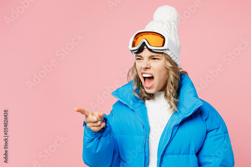 Snowboarder sad woman wear blue suit goggles mask hat ski padded jacket point index finger aside on area isolated on plain pastel pink background Winter extreme sport hobby weekend trip relax concept