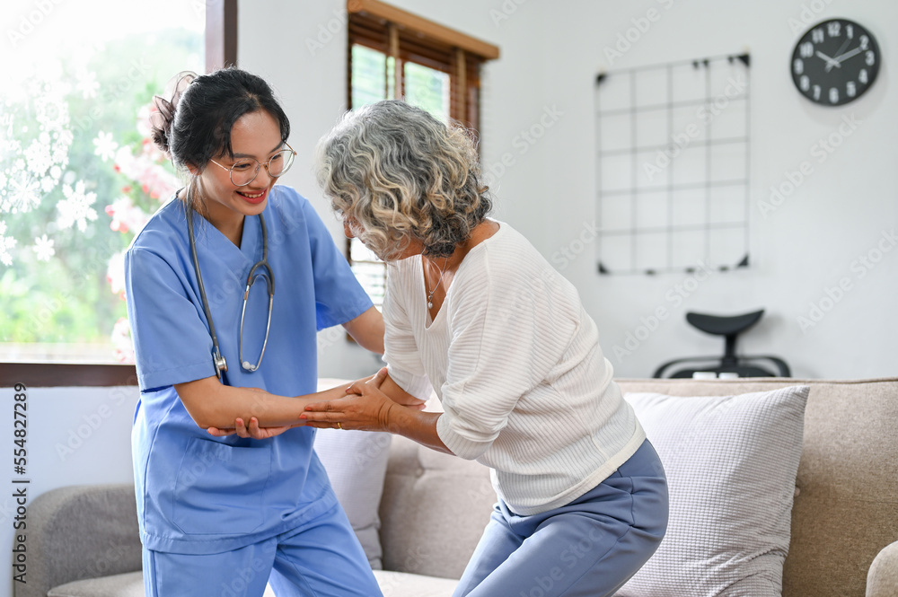 Fototapeta premium A 60-year-old elderly retire woman being helped by a young female nurse to standup and walk.