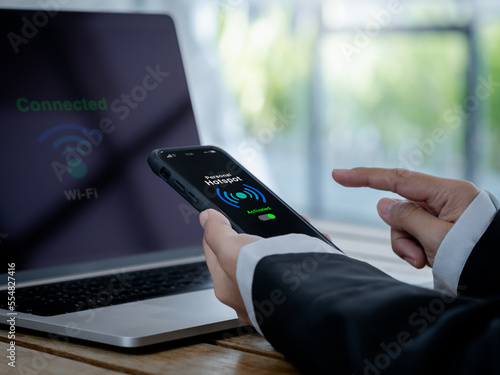personal hotspot technology concept. The words personal hotspot, internet sharing icon and green activated button on mobile smart phone screen in hand, connecting wi-fi network to laptop computer.