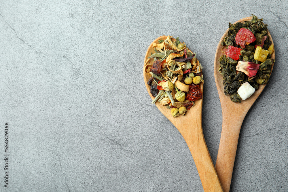 Different kinds of dry herbal tea in wooden spoons on light grey table, flat lay. Space for text Different kinds of dry herbal tea in wooden spoons on light grey table, flat lay. Space for text