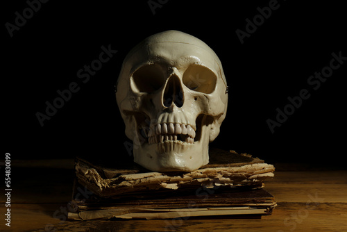 Human skull and old book on wooden table against black background