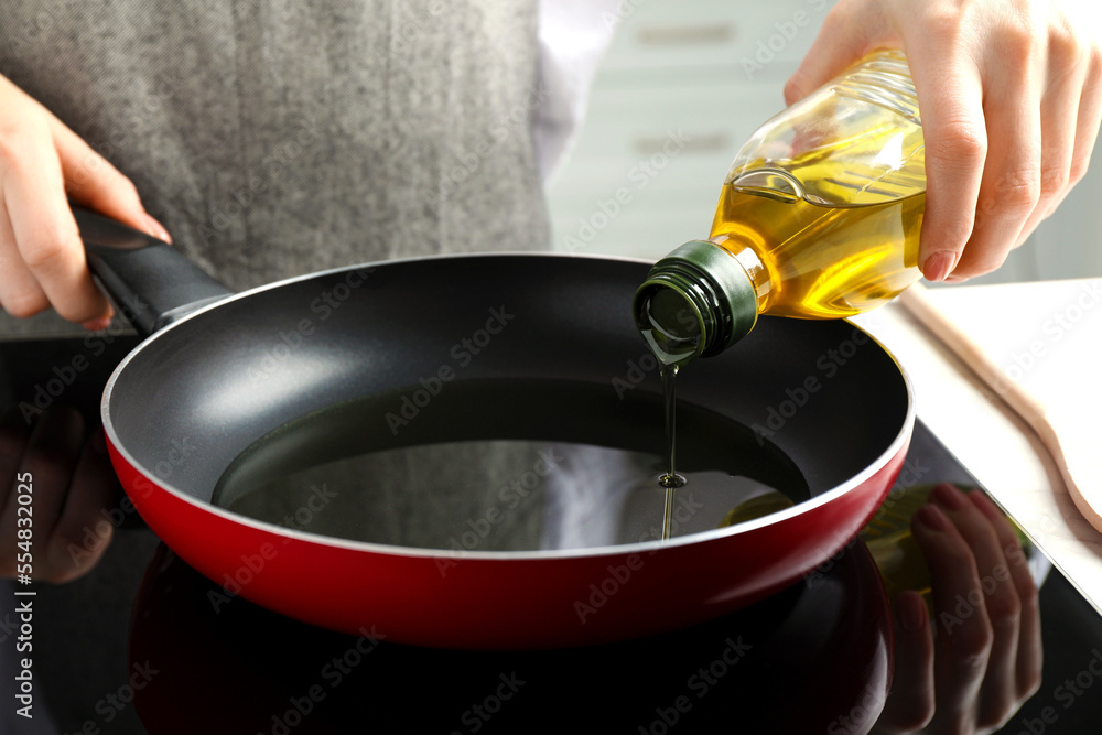 Woman pouring cooking oil from bottle into frying pan on stove, closeup Woman pouring cooking oil from bottle into frying pan on stove, closeup