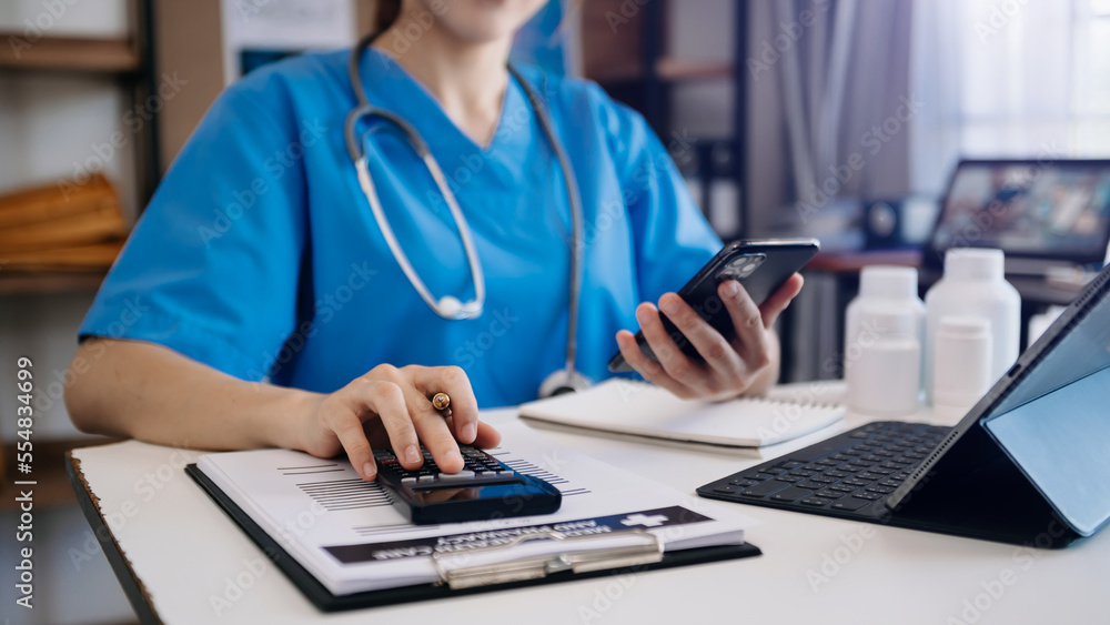 Healthcare costs and fees concept.Hand of smart doctor used a calculator and smartphone, tablet for medical costs at hospital in morning light Healthcare costs and fees concept.Hand of smart doctor used a calculator and smartphone, tablet for medical costs at hospital in morning light