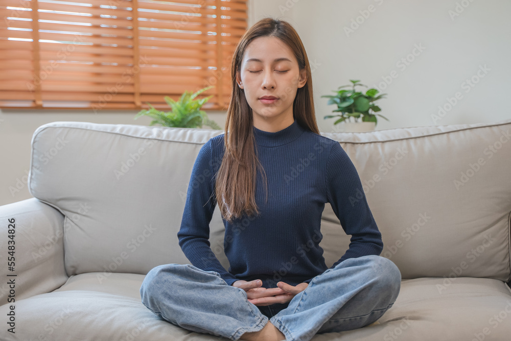 well being meditation. Asian women sit in the living room and practice mindfulness by focusing on breath concentrate.