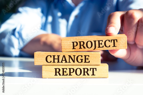 Closeup on businessman holding a wooden blocks with text PROJECT CHANGE REPORT, business concept