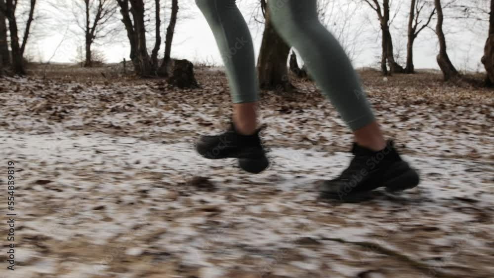 Close-up side view. Women's slim legs in sports leggings and sneakers run in a snowy winter park. Morning run in nature in winter Close-up side view. Women's slim legs in sports leggings and sneakers run in a snowy winter park. Morning run in nature in winter