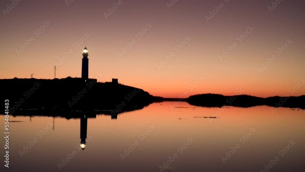 Shot Of Lighted Lighthouse At Clear Sky Night in Cadiz with the lighthouse reflected in the water Shot Of Lighted Lighthouse At Clear Sky Night in Cadiz with the lighthouse reflected in the water