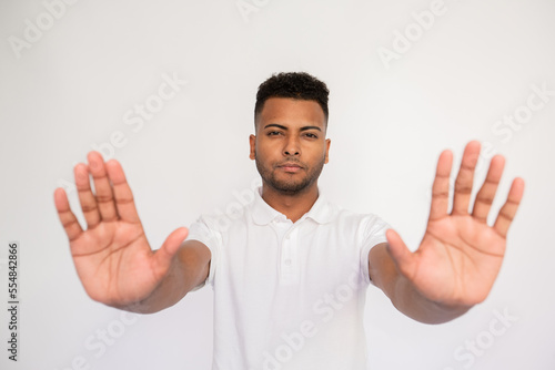 Serious young man showing stop signs. Male Indian model with brown eyes and curly hair in casual clothes showing his palms as stop signs. Forbiddance, advertising concept