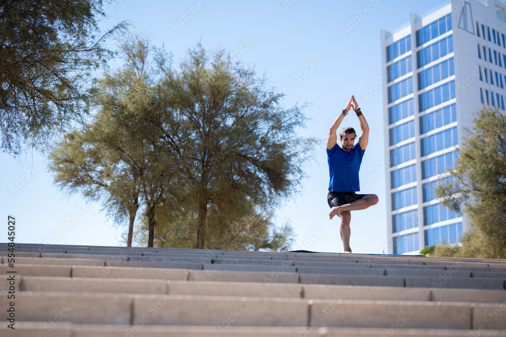 Young man with beard and ponytail performing balancing exercises in an urban environment. Sports concept.